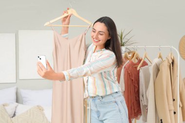 Şık elbiseli ve cep telefonlu genç bir kadın yatak odasında selfie çekiyor.