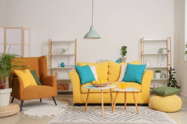 Güzel oturma odasının içinde sarı kanepe, sehpa, koltuk ve raf ünitesi.