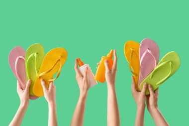 Yeşil arka planda parmak arası terlik ve güneş kremi olan kadın elleri.