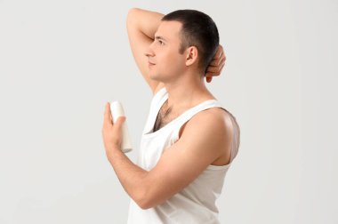Gri arka plana deodorant süren yakışıklı genç adam.