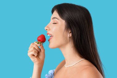 Güzel genç bayan mavi arka planda taze çilek yiyor.