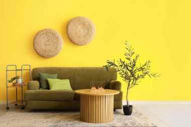 İçinde yeşil kanepe, sehpa ve zeytin ağacı olan güzel bir oturma odası.