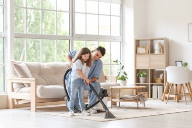 Genç baba ve kızı elektrikli süpürge ile evde birlikte halı temizliyorlar.