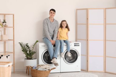 Genç baba ve kızı banyoda çamaşır makinesinde oturuyorlar.