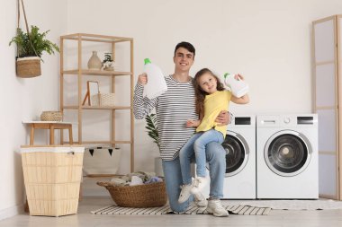 Genç baba ve kızı banyoda çamaşır deterjanı şişeleriyle