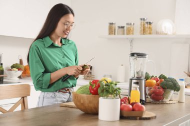 Genç Asyalı kadın mutfakta kivi kesiyor.