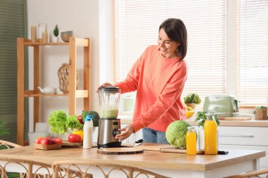 Mutfakta blenderlı genç bir kadın smoothie yapıyor.