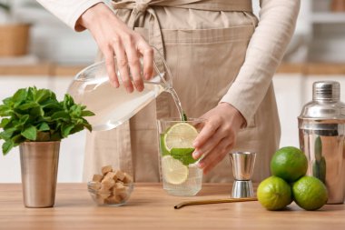 Genç bir kadın evinde bir bardak taze mojito ile su ekliyor.