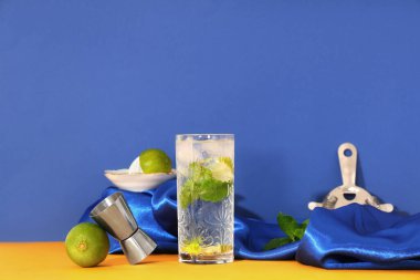 Bir bardak taze mojito, jigger ve limon ile turuncu masada mavi arka planda.