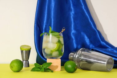 Beyaz arka planda sarı masada limonlu ve kokteylli bir bardak taze mojito.