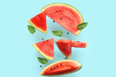 Uçan taze karpuz parçaları ve mavi arka planda nane ve tohumlar.