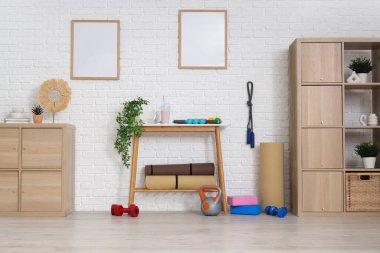 Odanın yanındaki beyaz tuğla duvarın yanında ahşap raf ve farklı spor aletleri.