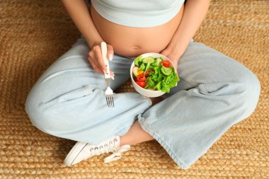 Evde bir kase taze sebze salatasıyla genç hamile kadın, yakın plan.