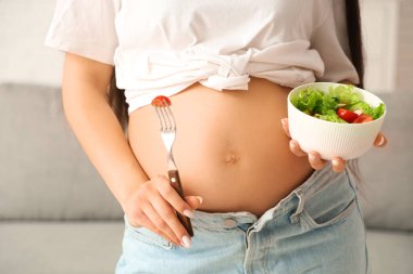 Evde bir kase taze sebze salatasıyla genç hamile kadın, yakın plan.
