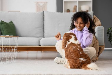 Kulaklıklı genç Afro-Amerikalı kız yerde tatlı süvari Kral Charles Spaniel ile oturuyor.