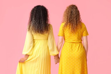 Pembe arka planda el ele tutuşan genç kadınlar.