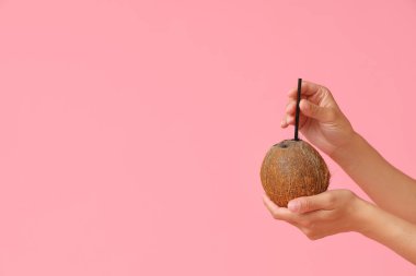 Pembe arka planda taze hindistan cevizi ve pipet olan kadın elleri.