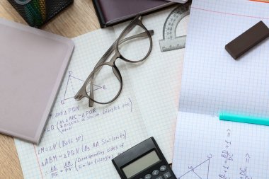 Matematik formüllü, gözlüklü ve ahşap masadaki kırtasiyeli metin kitapları, yakın plan.
