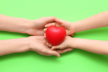 Yeşil arka planda kırmızı kalpli kadın ve çocuğun elleri, yakın plan.