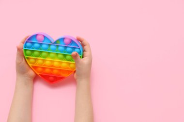 Pembe arka planda oyuncak kalp şeklinde çocuk elleri, yakın plan.