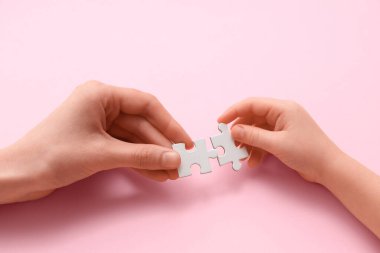 Pembe arka planda yapboz parçaları olan kadın ve çocuk elleri, yakın plan.