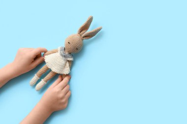 Renkli arka planda örülmüş oyuncak tavşanı olan çocuk elleri