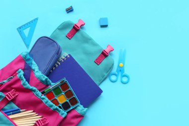 Mavi arka planda farklı kırtasiye malzemeleriyle modern okul sırt çantası.