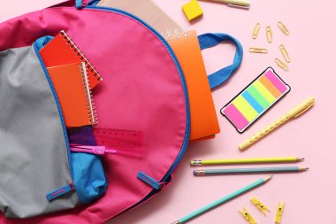 Okul çantasında pembe arka planda farklı kırtasiye malzemeleri var.