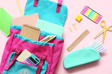 Pembe arka planda farklı kırtasiye malzemeleriyle modern okul çantası.