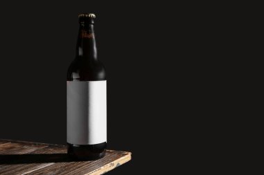 Siyah arka planda, tahta masada bir şişe soğuk bira.