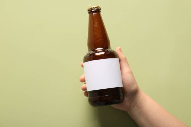 Yeşil arka planda soğuk bira şişesi olan bir kadın eli.