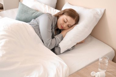 Evde ilaç içtikten sonra yatakta uyuyan genç bir kadın.