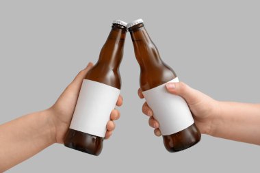Gri arka planda bira şişeleri tutan kadın eller.