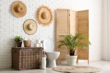 Tuvalet, çamaşır sepeti ve tuvalet odasındaki beyaz tuğla duvarın yanındaki katlı ekran.