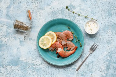 Lezzetli haşlanmış karides, limon ve açık mavi arka planda bir kase sos.