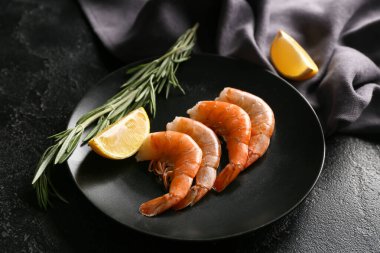 Lezzetli haşlanmış karides, limon ve biberiye ve siyah arka planda.