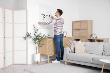 Evdeki ışık duvarına poster asan genç adam.