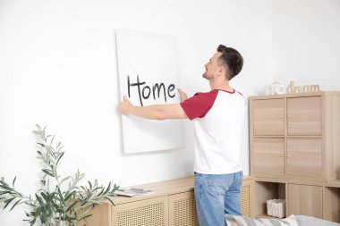 Evdeki ışık duvarına poster asan genç adam.