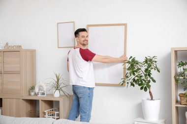 Evdeki ışık duvarına boş bir çerçeve asan genç adam.