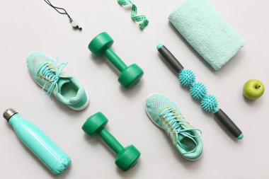 Spor ayakkabıları, elma, mezura ve gri arka planda farklı spor aletleri.