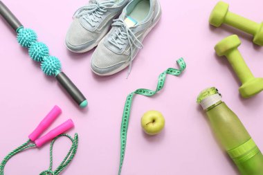 Pembe arka planda spor ayakkabıları, elma ve spor aletleri