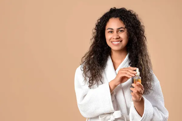 stock image Beautiful young happy African-American woman with healthy curly hair and care oil on beige background