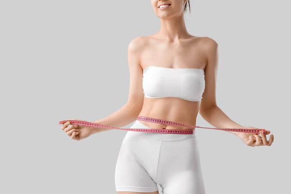 Молодая счастливая женщина спортивного телосложения со скотчем на сером фоне, приподнятая. Концепция потери веса