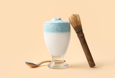 Bir bardak mavi dalgona matcha latte, ahşap kaşık ve bej arka planda chasen.