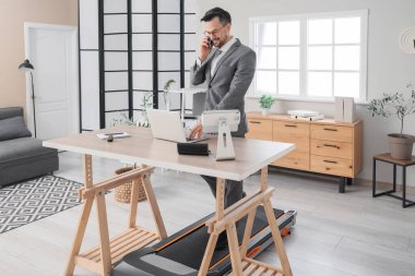 Ofisteki koşu bandında cep telefonuyla konuşan yakışıklı bir iş adamı.