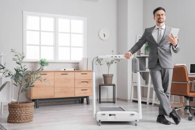 Ofiste koşu bandının yanında tablet bilgisayarı olan yakışıklı bir iş adamı.