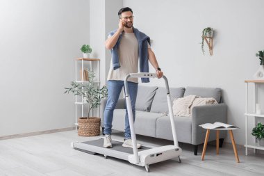 Evde koşu bandında cep telefonuyla konuşan yakışıklı bir işadamı.