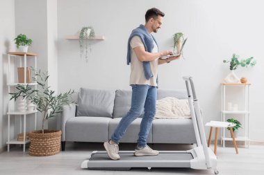 Evde koşu bandında dizüstü bilgisayarla çalışan yakışıklı bir iş adamı.