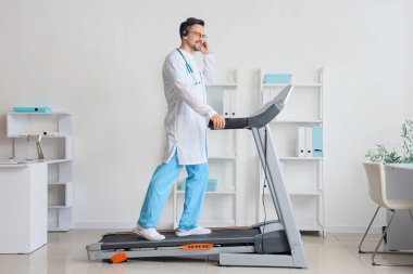 Hastanede koşu bandında çalışan kulaklıklı bir erkek doktor.