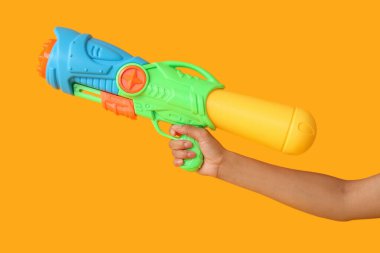 Sarı arka planda su tabancası olan bir kadın eli.